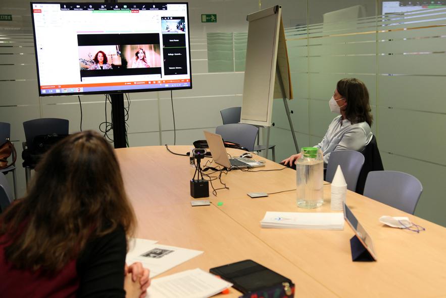 II Jornadas de Mediación Ciudad de Alcobendas -  Panorámica de una sala de reuniones con tres participantes, con mascarillas y la pantalla con una conferencia on line.