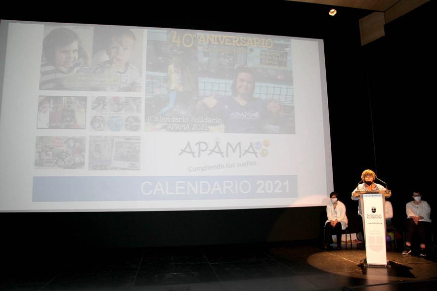 Presentación Calendario APAMA 2021 - Imagen de una mujer dirigiéndose al público asistente mientras en la pantalla vemos imágenes del calendario.