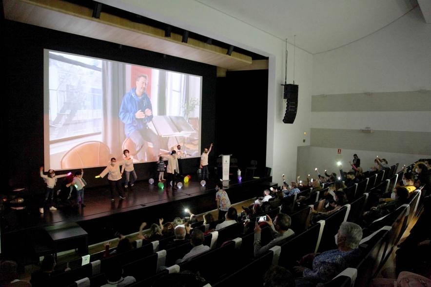 Presentación Calendario APAMA 2021 - Imagen panorámica, vemos el escenario donde vemos actuando a unas personas y al público asistente.