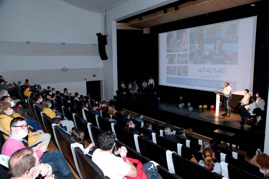 Presentación Calendario APAMA 2021 - Imagen panorámica, vemos el escenario donde vemos actuando a unas personas y al público asistente.