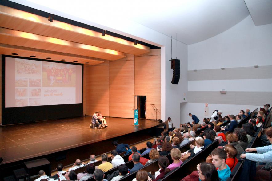 Presentación Calendario APAMA 2019 - Panorámica de los espectadores del teatro y el escenario con  un niño en sillas de ruedas  y su padre.