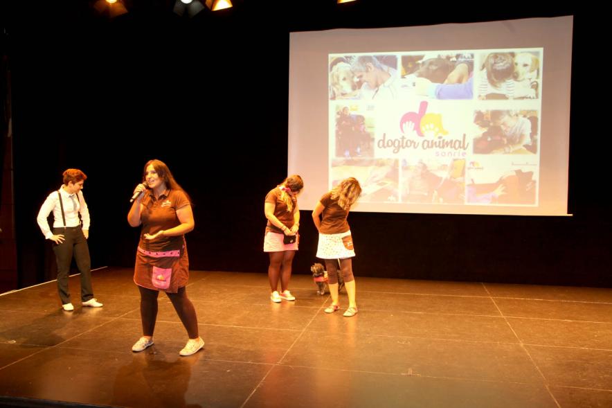 Presentación Curso Escolar 2019-20 APAMA -   Imagen del escenario con un grupo de  monitoras de APAMA, con los perros de las terapias. 