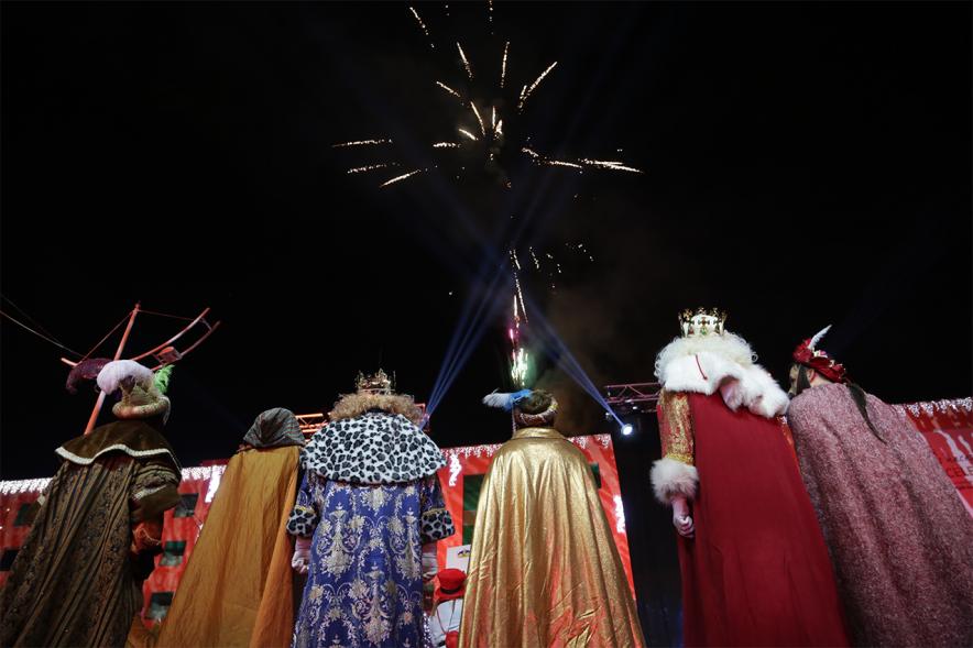 Cabalgata de Reyes 2019 -  Imagen de los tres Reyes Magos en el escenario acompañados de sus respectivos pajes mirando hacia el cielo donde podemos ver los fuegos artificiales.