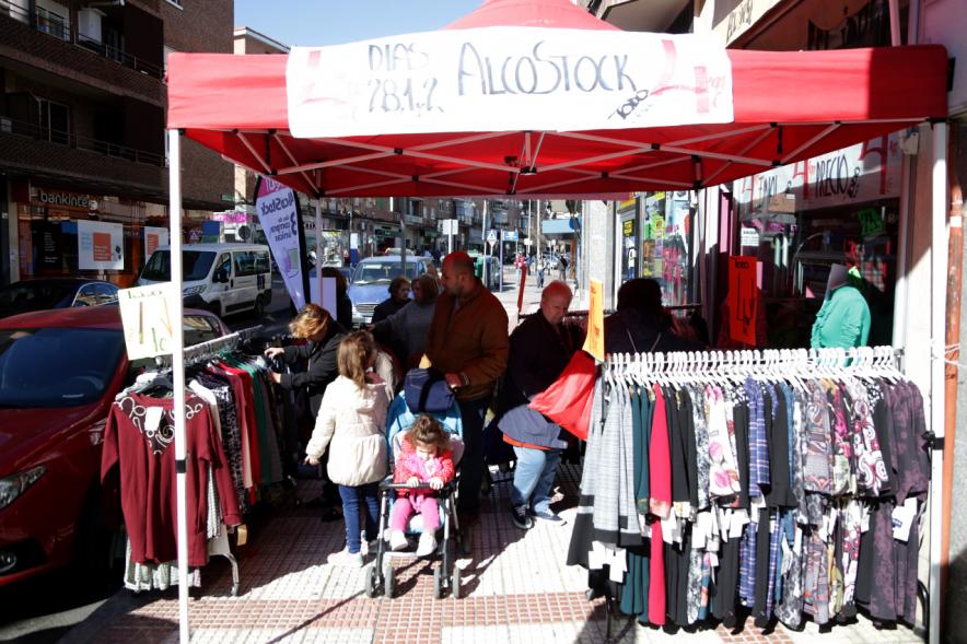 Visita Tiendas Alcostock 2019 -  Imagen de varias personas mirando los percheros que hay montado en el exterior de una de las tiendas participantes en la feria.