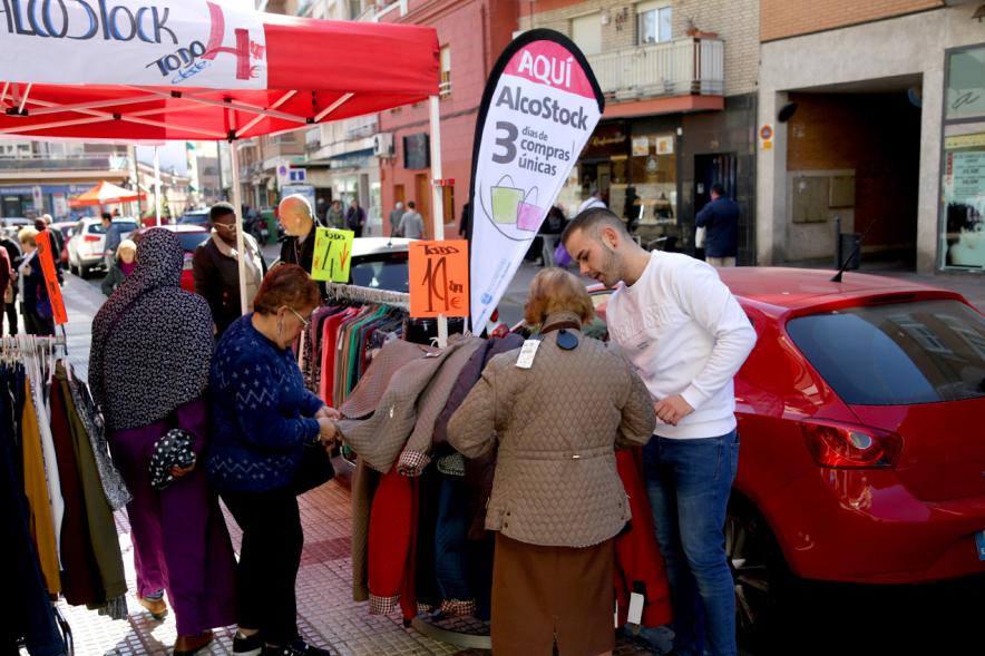 Visita Tiendas Alcostock 2019 - Imagen de varias personas mirando el mostrador que hay montado en el exterior de una de las tiendas participantes en la feria.