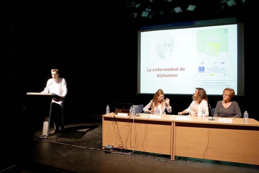 Día Mundial del Alzehimer - Imagen de un momento de la charla de un conferenciante y de otras conferenciantes en la mesa siguiendo la charla.