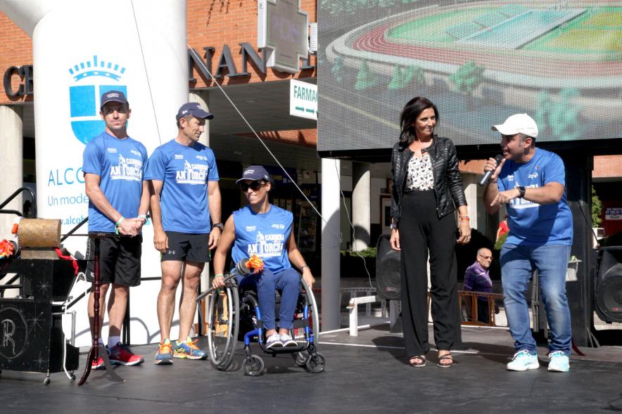 Carrera de la Antorcha Olímpica - Imagen atleta paralímpico con la llama olímpica y otras personas en el escenario.