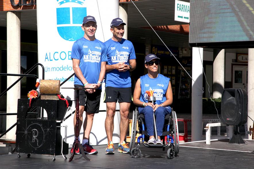 Carrera de la Antorcha Olímpica - Imagen atleta paralímpico con la llama olímpica y otras personas en el escenario.