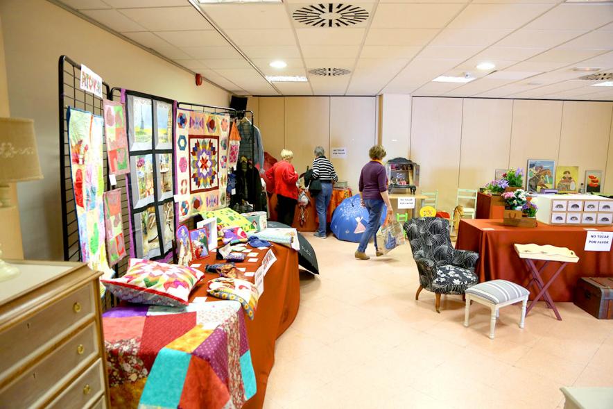 Exposición Asociación de Artesanas de Alcobendas - Panorámica de la exposición con todos los productos artesano  y varios visitantes.