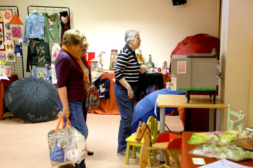 Exposición Asociación de Artesanas de Alcobendas - Imagen de los productos expuesto y dos visitantes observándolos.