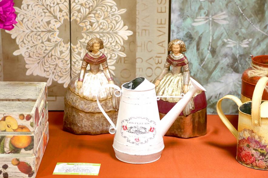Exposición Asociación de Artesanas de Alcobendas - Primer plano de una regadera y dos muñecas artesanales.