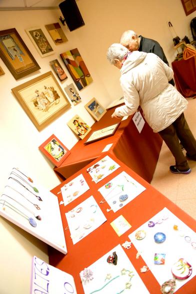 Exposición Asociación de Artesanas de Alcobendas - Imagen de la mesa con los  productos artesanos y varias visitas.