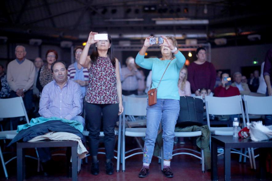 Semana Cultural Asturiana 2018 - Actuación Folk - Imagen de dos personas haciendo fotos con sus móviles al grupo de música que esta actuando en el escenario.