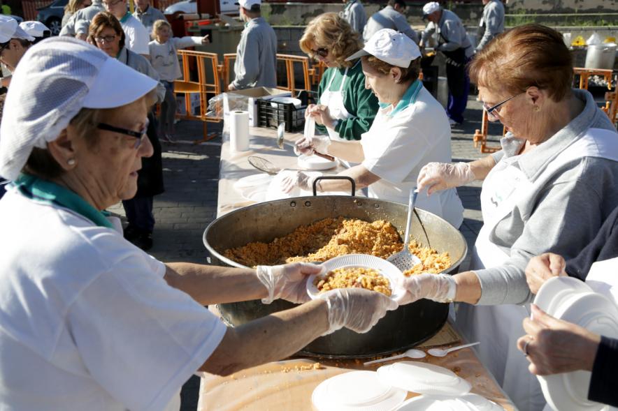 Paellada popular con detalle de mujer sirviendo un plato