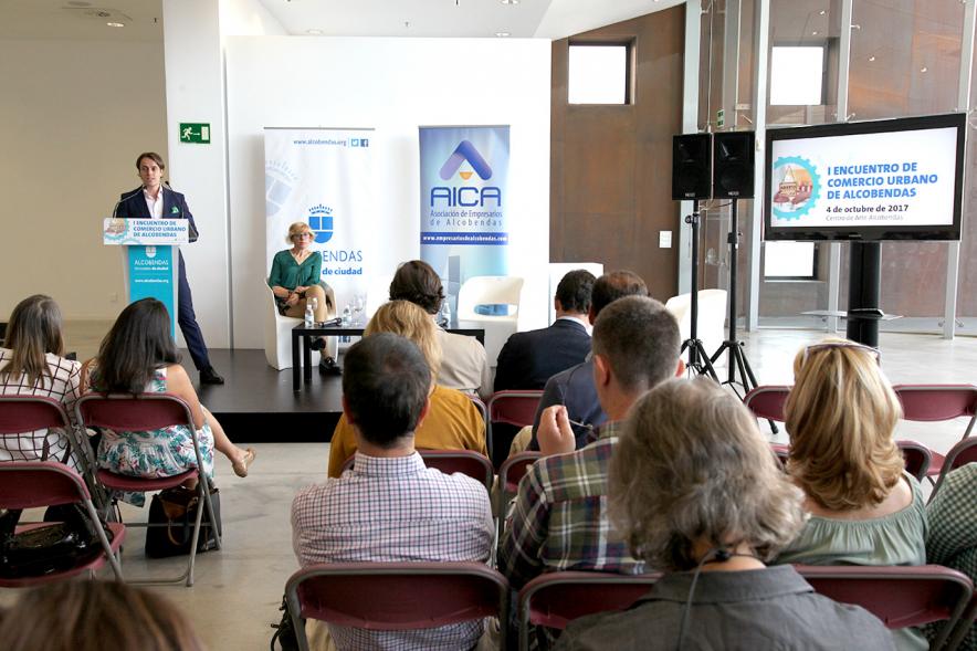 Ier Encuentro de Comercio Urbano de Alcobendas - Imagen panorámica del lugar donde se celebra el encuentro, personas asistentes y oradores en el escenario.