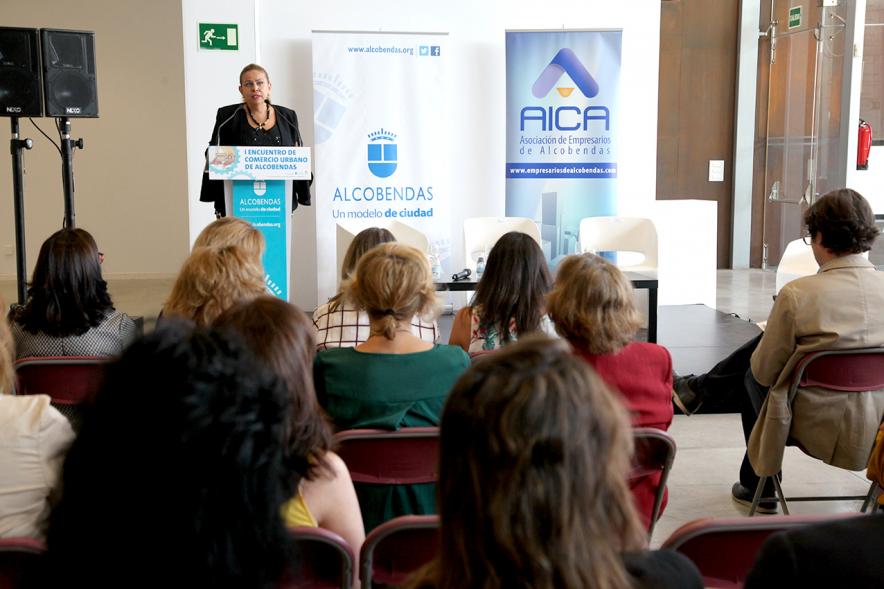 Ier Encuentro de Comercio Urbano de Alcobendas - Imagen panorámica del lugar donde se celebra el encuentro, personas asistentes y una oradora en el escenario.