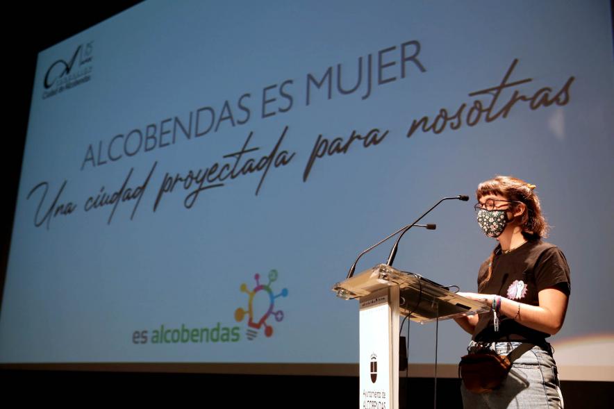 Semana contra la Violencia de Género - Encuentro con Oihane Ruíz - Primer plano de una joven dando un discurso junto a la proyección del cartel del encuentro.