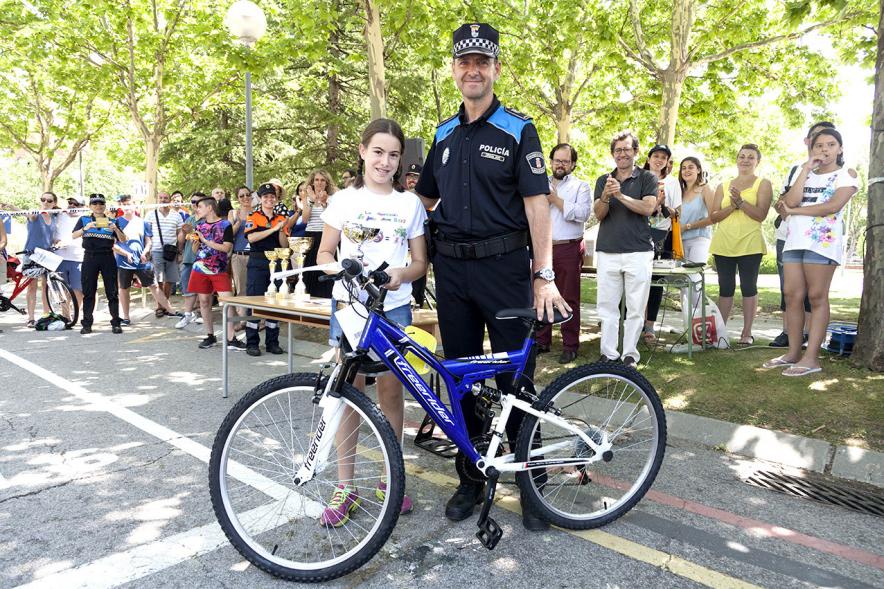 Entrega Premios XXIIº Concurso Escolar de Dibujo y Eslogan sobre Educaión y Seguridad Vial - Imagen de una niña premiada con una bicicleta junto una fuerza del orden asistente al acto.