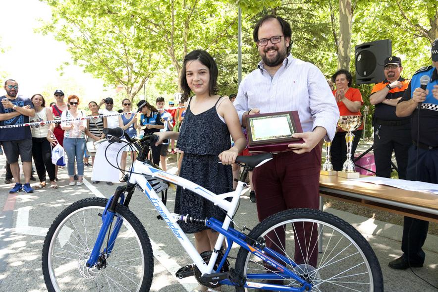 Entrega Premios XXIIº Concurso Escolar de Dibujo y Eslogan sobre Educaión y Seguridad Vial - Imagen de una niña premiada con una bicicleta junto con una autoridad asistente al acto.