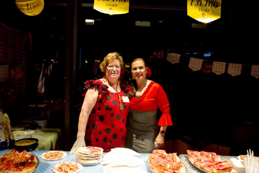Feria de Abril 2018 - Imagen de dos mujeres vestidas de andaluza delante de una mesa con tapas típicas de Andalucía.