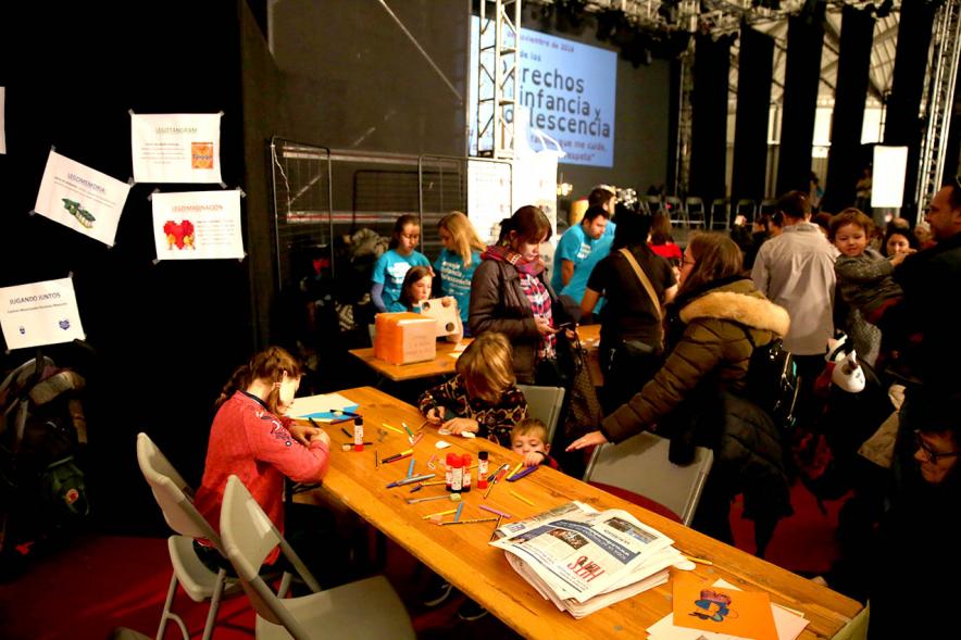 Fiesta Derechos de la Infancia - Primer plano de una niña  en una mesa de juegos y un grupo de mayores.