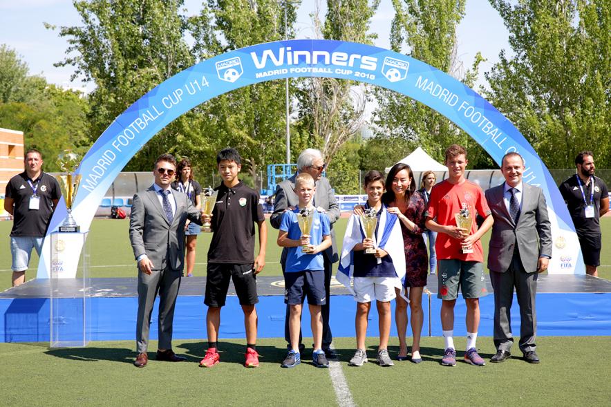 Torneo Internacional de Fútbol Madrid Football Cup U14 - Imagen de la entrega de trofeos, varios jugadores con sus trofeos de la mano  y las personas que los han entregado.