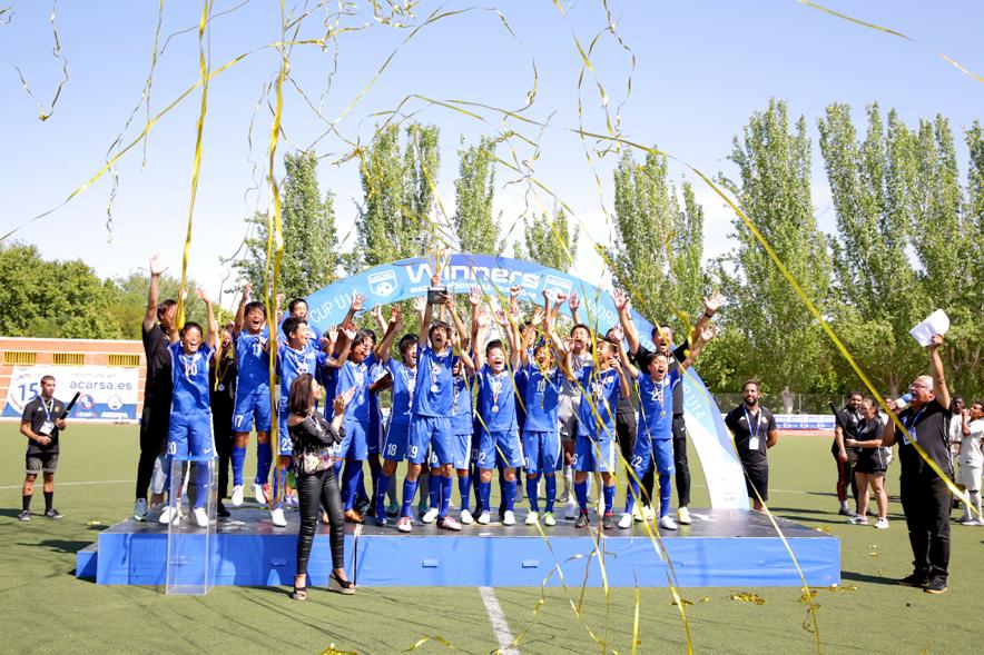 Torneo Internacional de Fútbol Madrid Football Cup U14 - Imagen del equipo gandador en el pódium celebrando la victoria, después de haber recibido el trofeo de ganador.