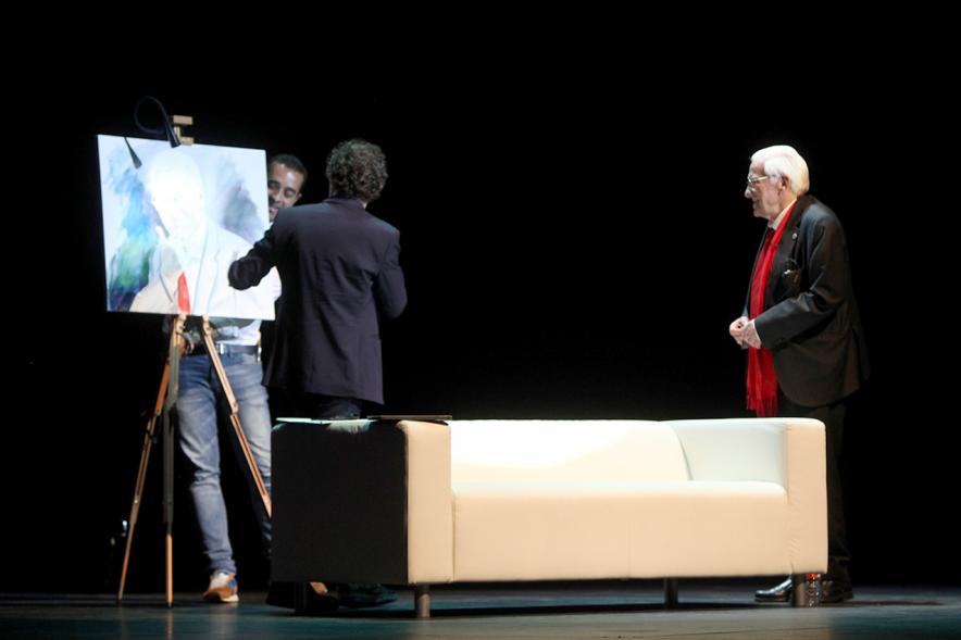 Gala Homenaje a la Solidaridad - Imagen del escenario, donde están sentados en un sofá charlando el mago More, el padre Angel y el pintor Víctor Jerez que realizó un retrato en el escenario del Padre Ángel.