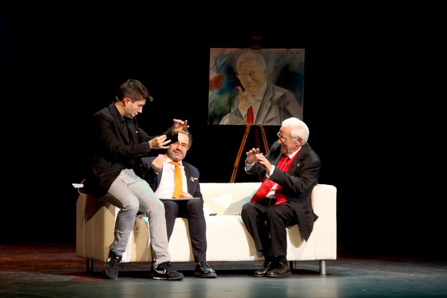 Gala Homenaje a la Solidaridad - Imagen del escenario, donde están sentados en un sofá charlando el mago More, el padre Angel y el pintor Víctor Jerez que realizó un retrato en el escenario del Padre Ángel.