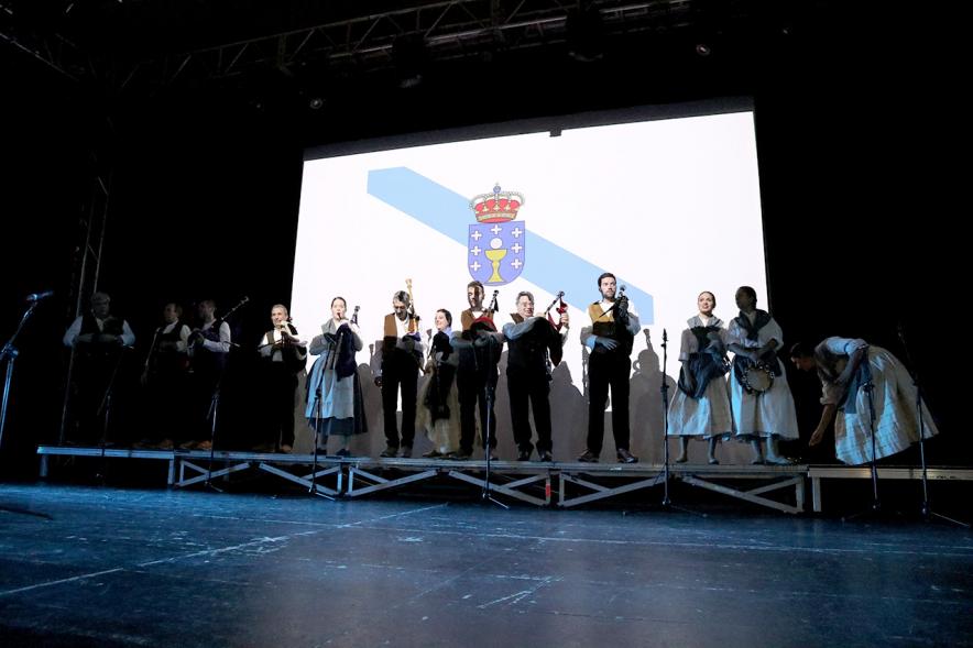 Día de Galicia 2018 - Imagen del escenario con el grupo musical regional y con la  bandera de fondo.