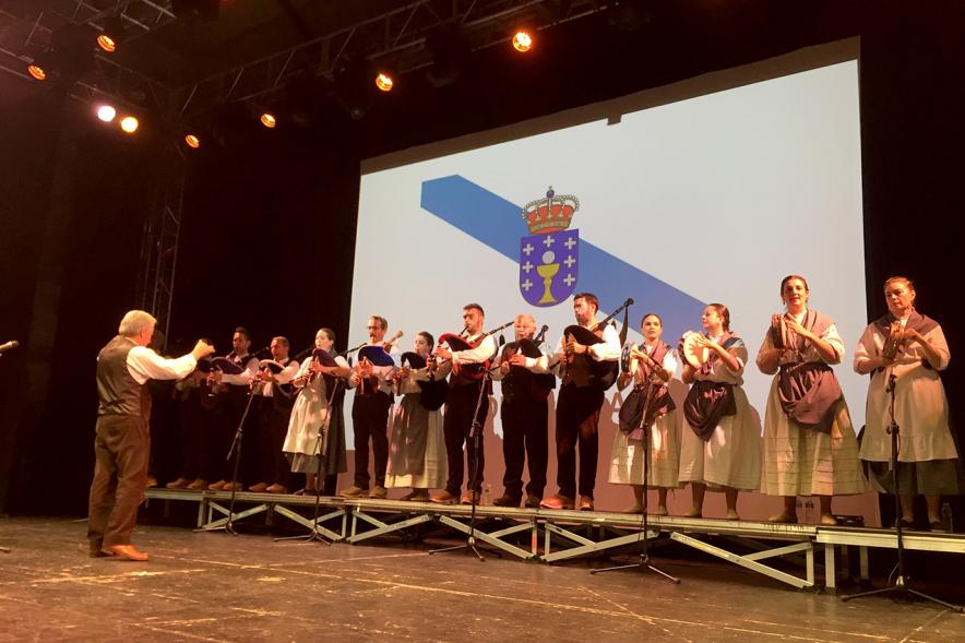 Día de Galicia 2018 - Imagen del escenario, el director  con el grupo musical regional y con la  bandera de fondo.