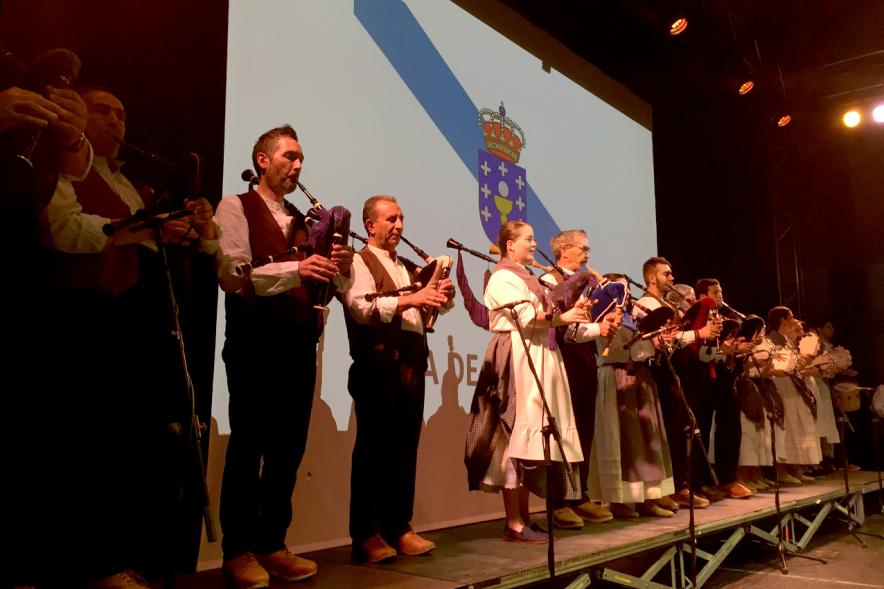 Día de Galicia 2018 - Imagen del escenario con el grupo musical regional y con la  bandera de fondo.
