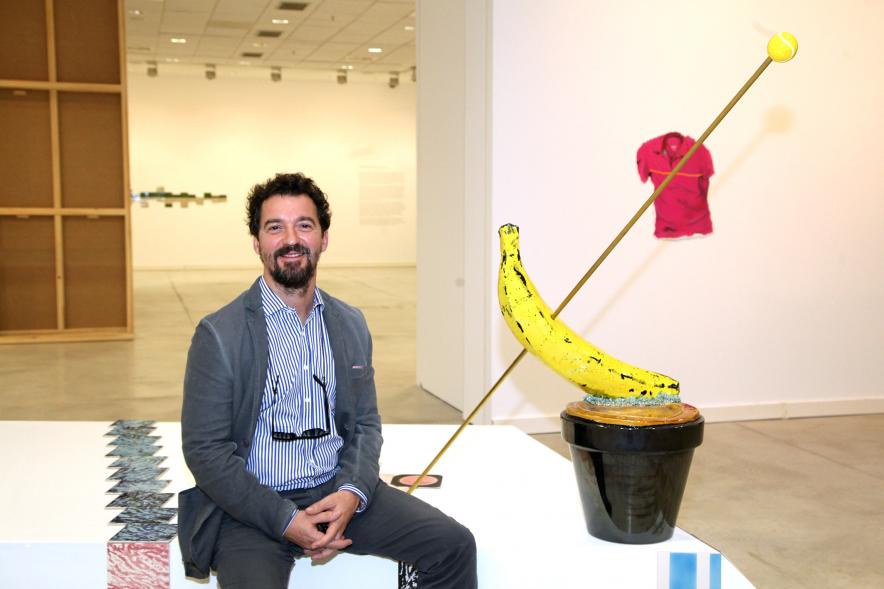 Inauguración de las Exposiciones "El camino Indicado" de Eduardo Barco y "Cocodrilos en la Pista - Estudio para una pieza Camp" de Miki Leal - Posado de Miki Leal junto a una composición artística, un cubo y un plátano.