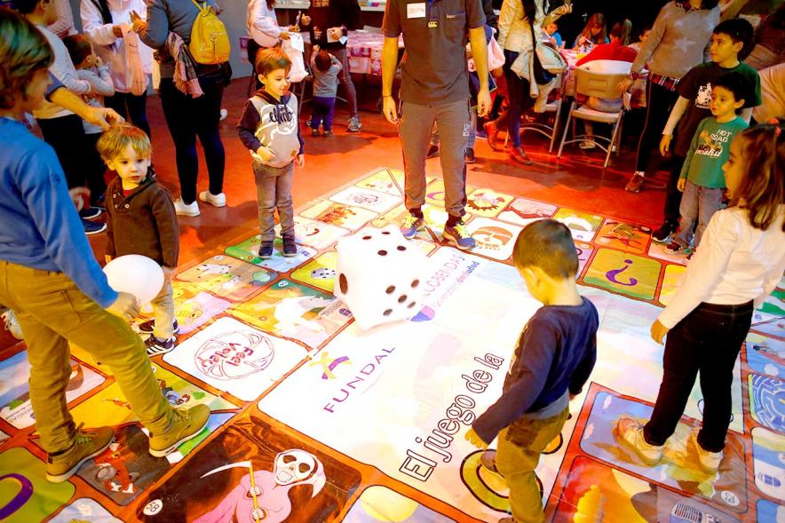 Fiesta Celebración Día Internacional de los Derechos de la Infancia - Imagen de un monitor jugando con unos niños al juego de la oca gigante.