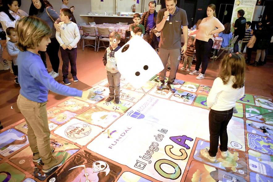 Fiesta Celebración Día Internacional de los Derechos de la Infancia - Imagen de un monitor jugando con unos niños al juego de la oca gigante.