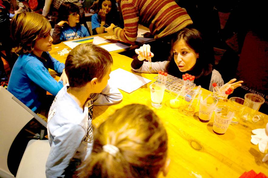 Fiesta Celebración Día Internacional de los Derechos de la Infancia - Imagen de una monitora realizando un pequeño experimento con unos niños.