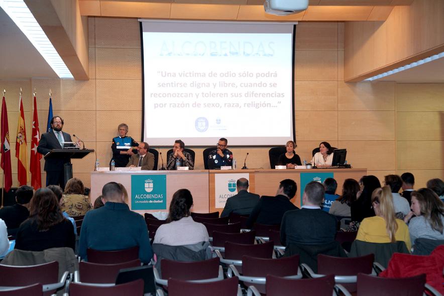 Clausura Jornada "Las Infracciones de Odio" - Imagen lejana del escenario con una autoridad dirigiéndose al público asistente y los componentes de la mesa de debate.