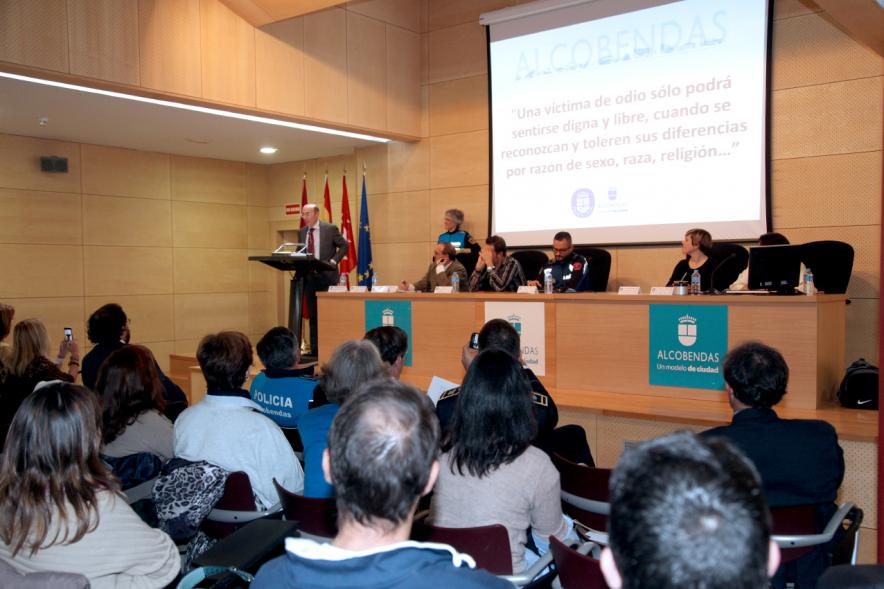 Clausura Jornada "Las Infracciones de Odio" - Imagen lejana del escenario con una autoridad dirigiéndose al público asistente y los componentes de la mesa de debate.