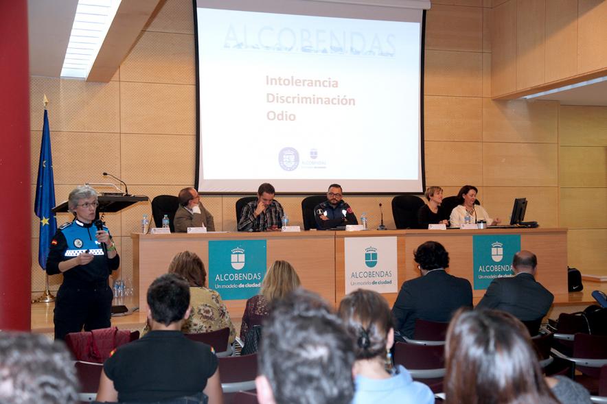 Clausura Jornada "Las Infracciones de Odio" - Imagen del escenario con un miembro de seguridad dirigiéndose al público asistente y los componentes de la mesa de debate.