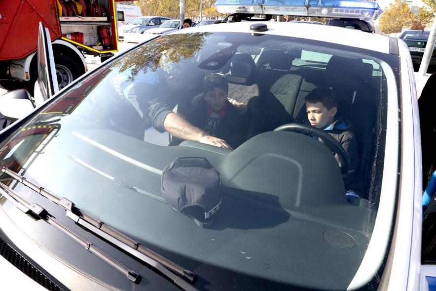 Jornada de Emergencias en Familia - Imagen de un miembro de un cuerpo de seguridad con un niño enseñándole un coche patrulla.