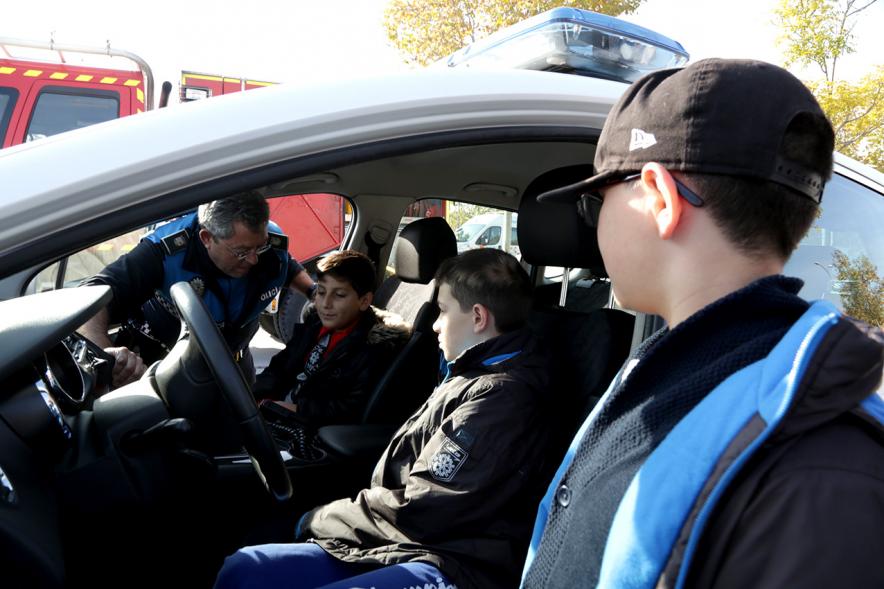 Jornada de Emergencias en Familia - Imagen de un miembro de un cuerpo de seguridad con un niño enseñándole un coche patrulla.