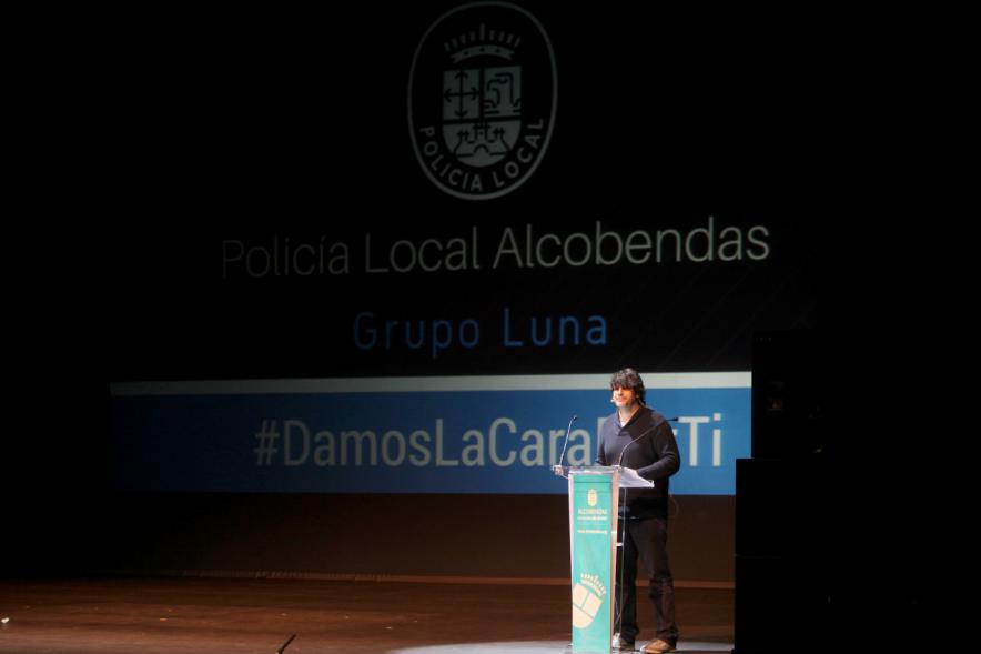 Jornada con los Institutos de Educación Secundaria Contra la Violencia de Género - Plano del escenario a media luz  y uno de los ponentes en el atril.