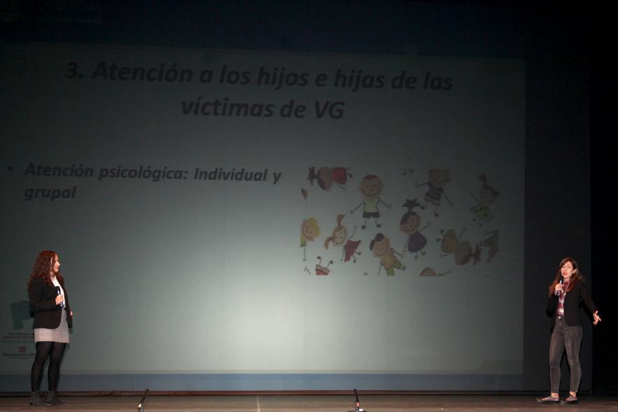 Jornada con los Institutos de Educación Secundaria Contra la Violencia de Género - Imagen del escenario con dos ponentes y parte de un informe de género.