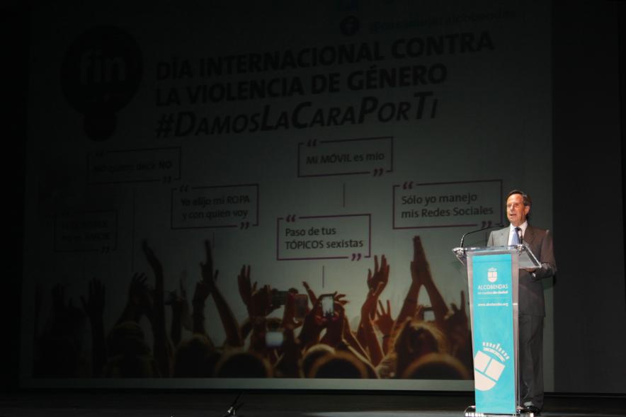 Jornada con los Institutos de Educación Secundaria Contra la Violencia de Género - Plano del  escenario con la diapositiva del evento  junto al alcalde García de Vinuesa desde el atril.