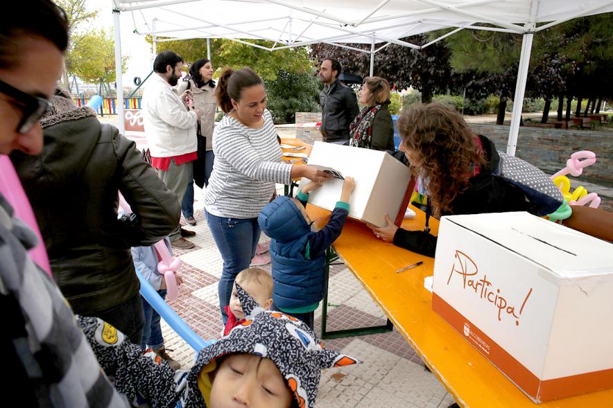 Proceso Participativo Elección de Luces Navideñas 2018 - Imagen  de las mesas con las urnas y una familia votando.