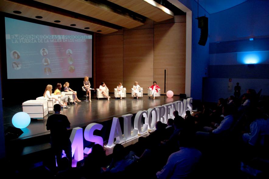 Media StartUps Alcobendas - Panorámica del escenario iluminado  con las ponentes sentadas. 
