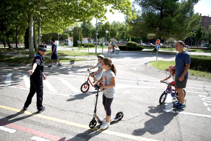 Semana Europea de la Movilidad - Tu Seguridad No Es Un Juego - Imagen de una policía municipal dirigiendo a unas niñas en patinete.