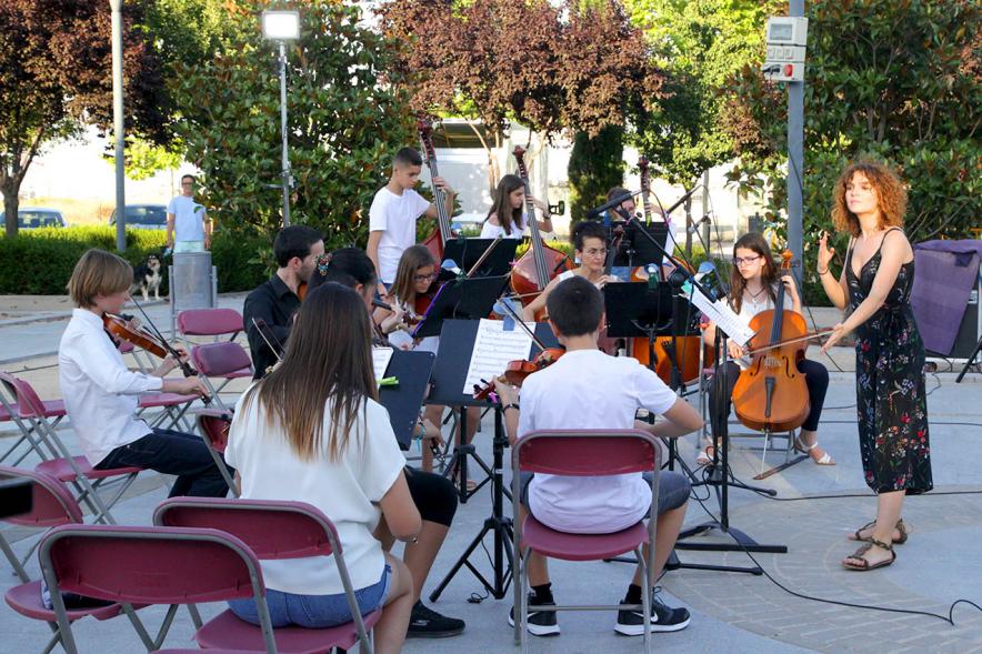 La Música Conquista la Calle - Avda Pablo Iglesias -Imagen de unos jóvenes tocando diferentes instrumentos de cuerda y una directora de orquesta que les dirige.
