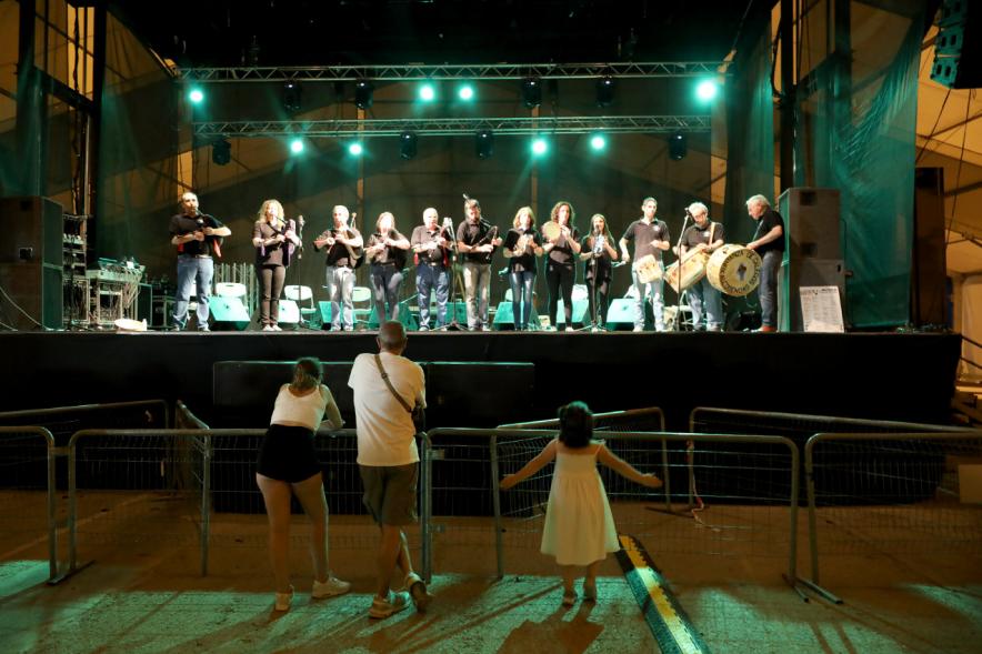 Noche de San Juan 2018 - Música a la Carpa - Imagen de un un grupo folk en el escenario y una personas en primera fila disfrutando de su música.