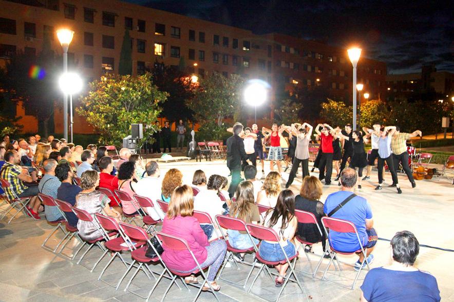 La Música Conquista la Calle - Avda Pablo Iglesias - Imagen de público asistente al evento y unos jóvenes en el escenario, donde se están haciendo una especie de danza y les dirige una persona.